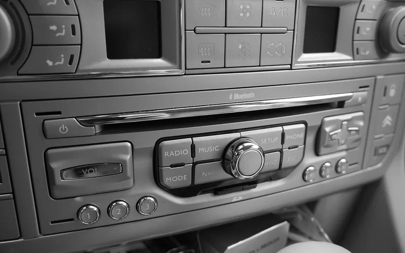 Factory car stereo faceplate with Bluetooth branding and physical buttons in a dashboard Factory car stereo faceplate with Bluetooth branding and physical buttons in a dashboard