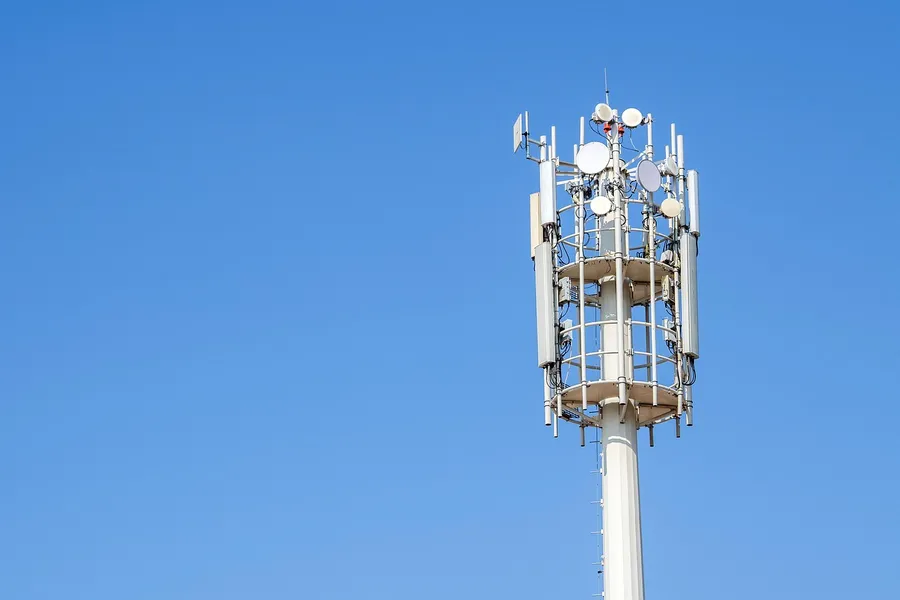 Communications tower carrying panel antennas and dishes against a blue sky