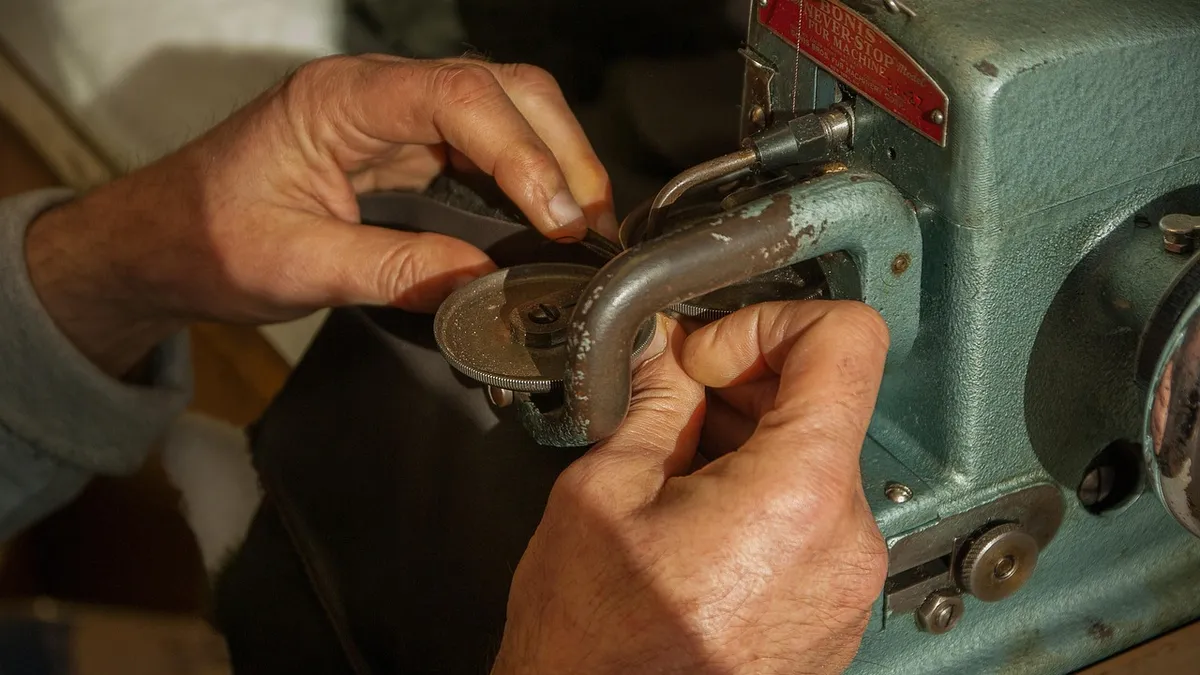 Hands using a curved needle to hand-stitch a leather seam repair