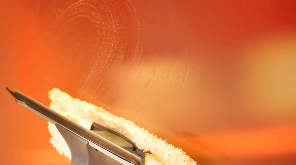 Hand holding a sponge squeegee wiping a soapy glass pane