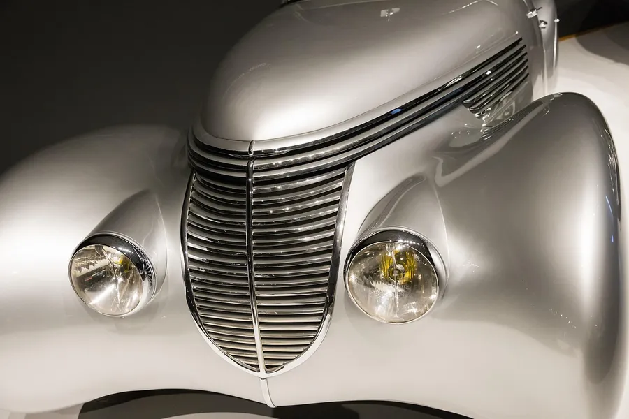 Polished silver classic car front with curved body panels around round headlamps and a vertical grille