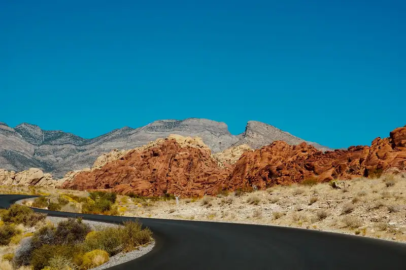 An empty desert highway with red rock hills under a blue sky