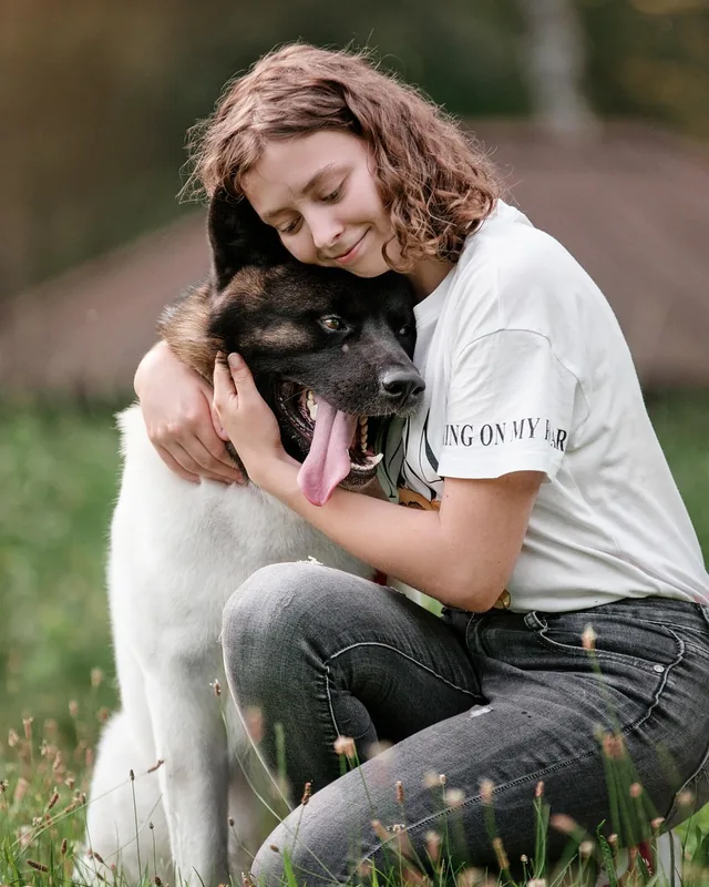 Young woman hugging a white and dark-faced dog on grass