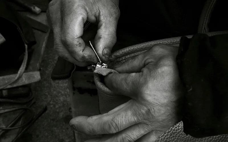 Hands working a needle through a leather item during a repair