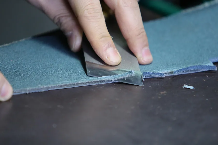 Hands trimming the edge of a leather strip with a blade
