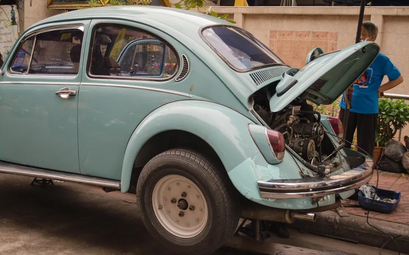 Light blue car with its engine lid open while a person stands nearby during a repair
