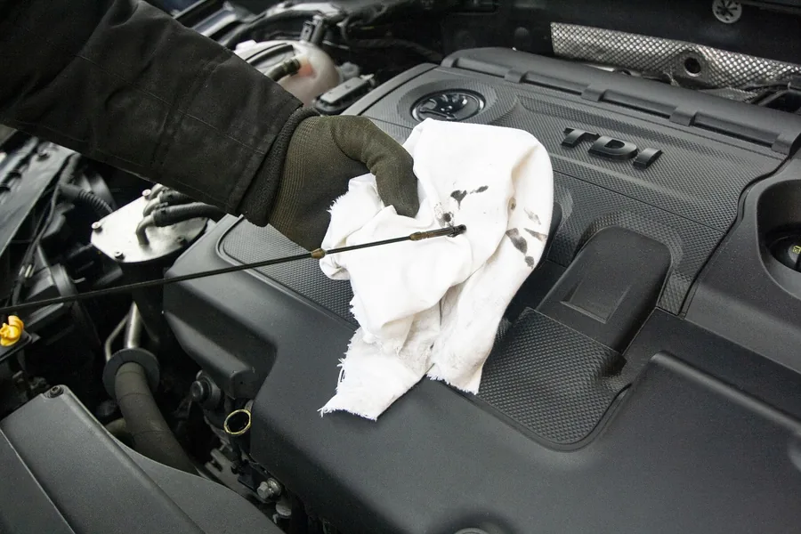 A mechanic checking engine oil with a dipstick under the hood A mechanic checking engine oil with a dipstick under the hood