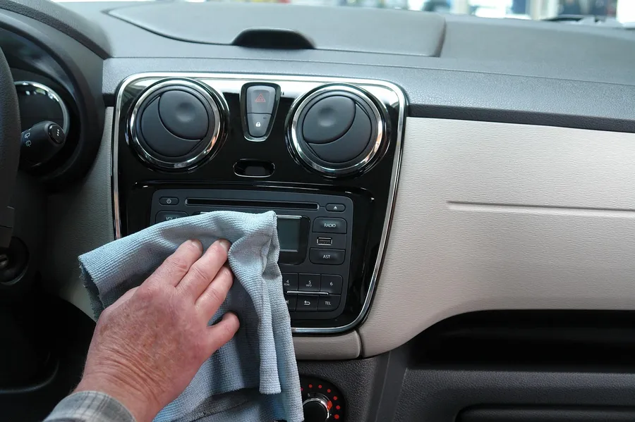Hand holding a gray microfiber cloth wiping a car interior panel