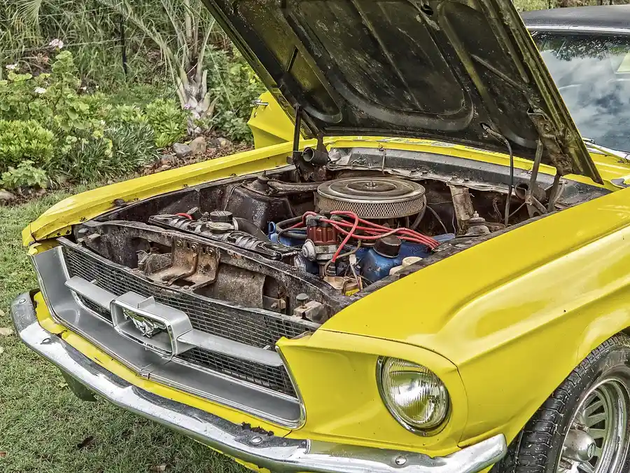 Open hood showing the engine bay of a yellow classic car parked on grass