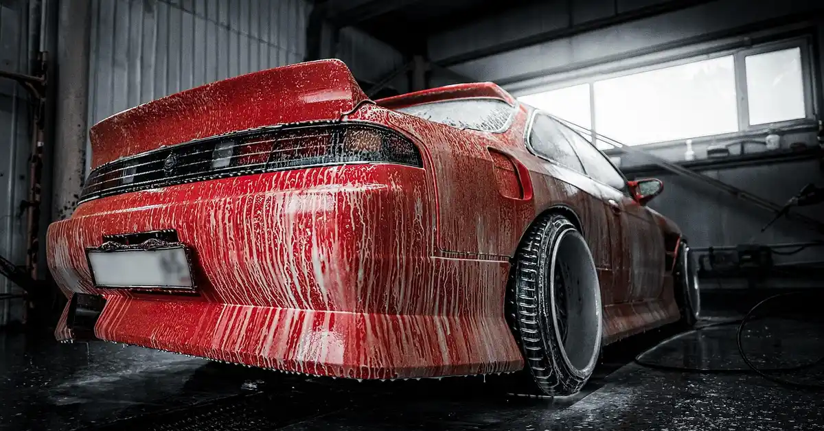 Red car covered in soap foam in a wash bay