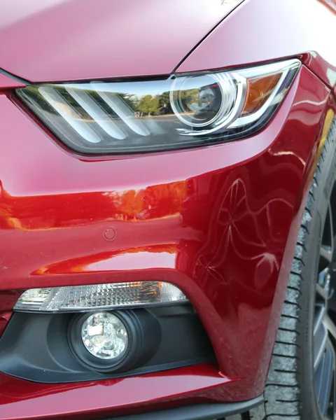Front corner of a red car showing the headlight with a separate fog lamp below it