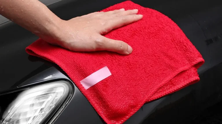 Hand pressing a damp red microfiber cloth on a dark car hood