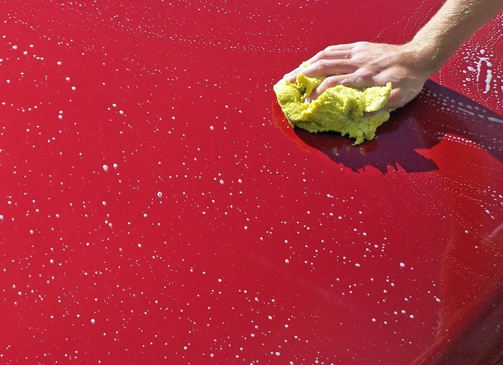 Hand working an applicator over one section of red car paint