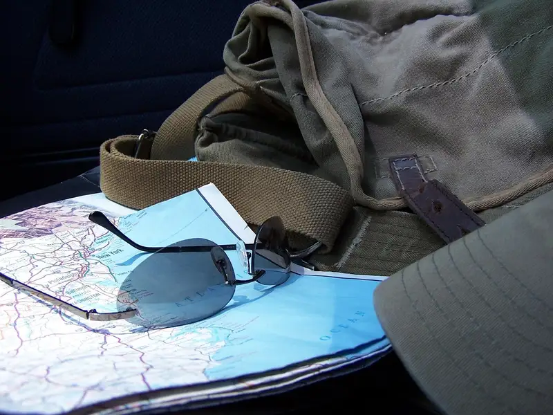 A folded road map with sunglasses, a bag and a cap on a car seat