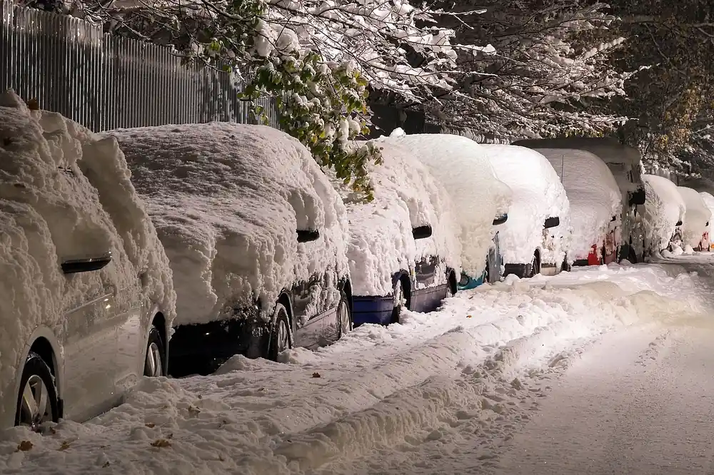 Row of parked cars buried under deep snow on a street at night