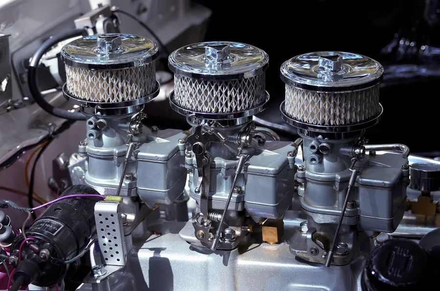 Three carburetors topped with round air cleaner housings on a car engine