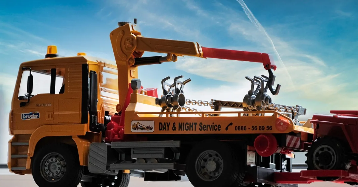 Flatbed tow truck towing a car on a road with hazard lights visible