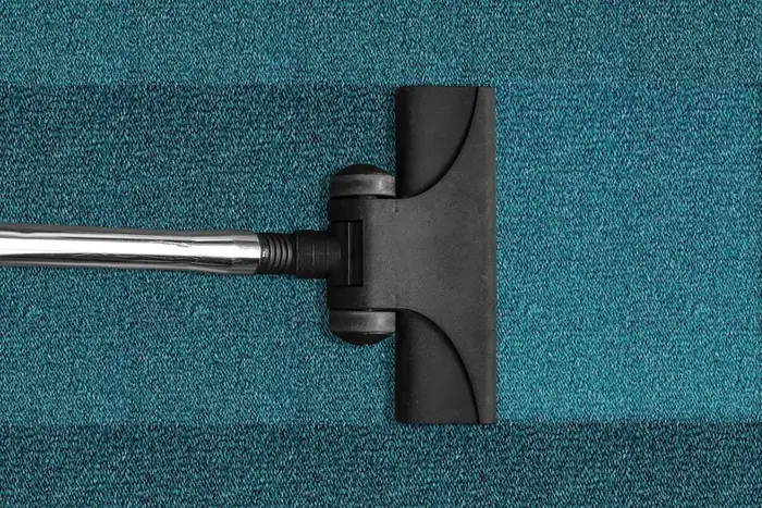 Vacuum cleaner head moving across a blue-green textile carpet