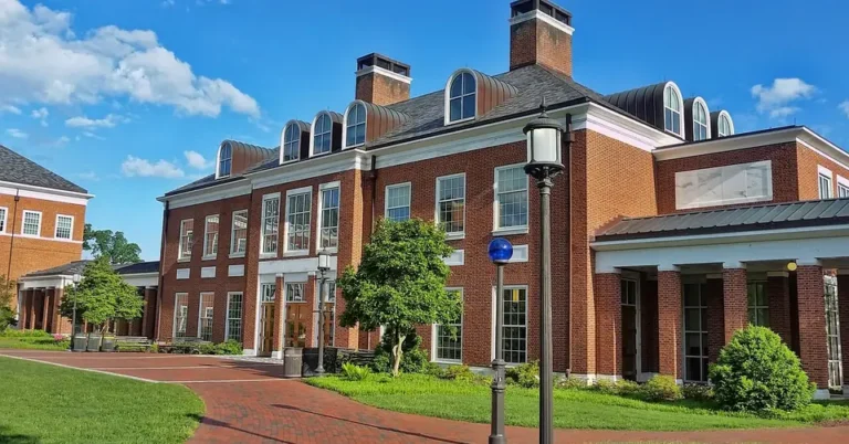 Red brick college building with dormer windows and a brick walkway under a blue sky