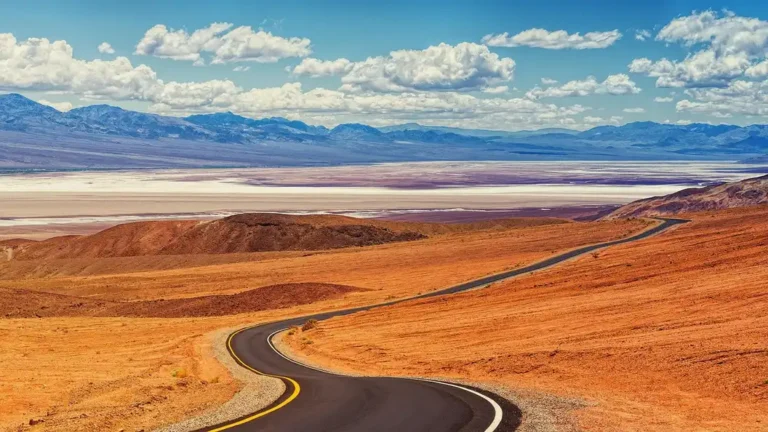 Winding desert highway under a blue sky with mountains in the distance