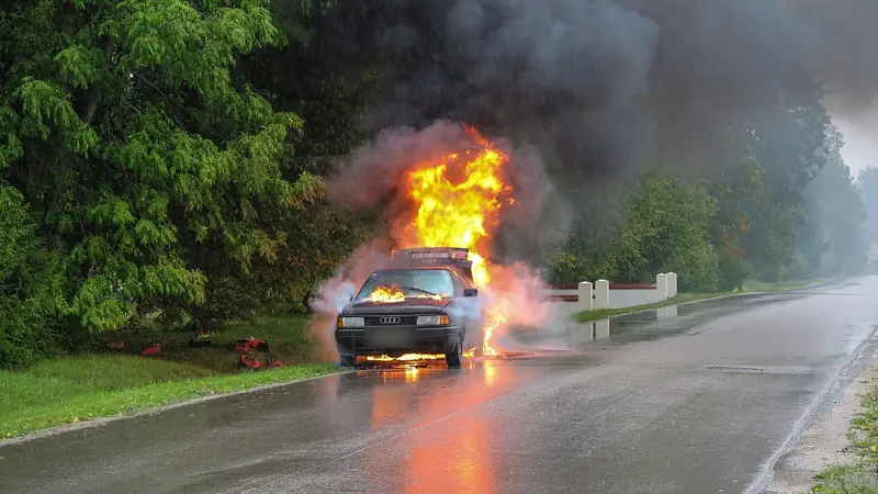 Car on fire on a wet road with flames and smoke rising