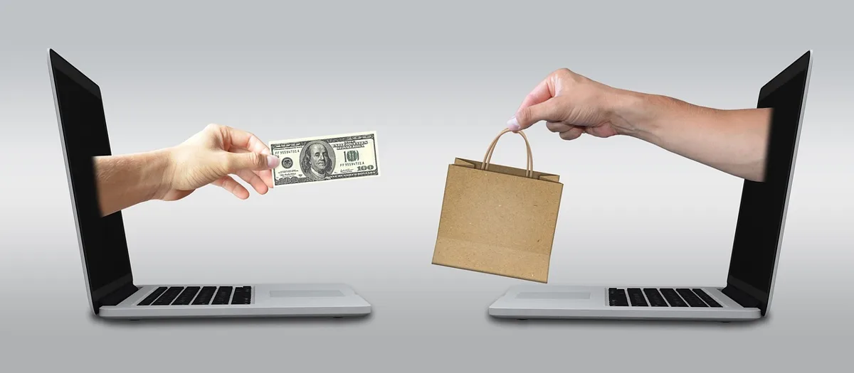 Two hands reaching out of laptop screens exchanging cash and a shopping bag