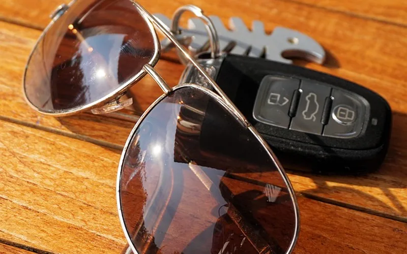 Black remote key fob with lock, unlock and trunk buttons lying next to sunglasses