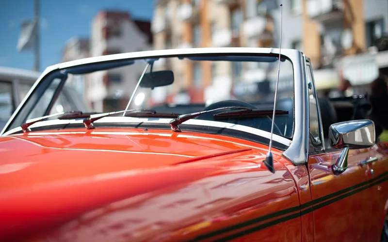Red classic convertible with its top down, hood and windshield in the foreground