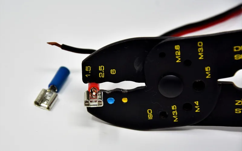 Crimping pliers holding a red-insulated terminal on a wire next to a spare blue terminal