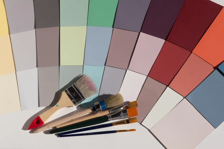 Fan of paint color swatches in grays, greens, pinks, reds and blues with several paint brushes lying on them