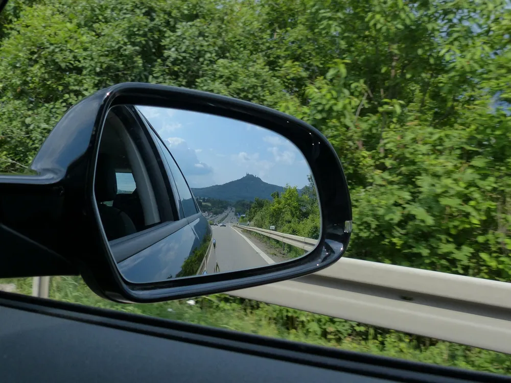 Black car side mirror showing the road and a hill behind the car