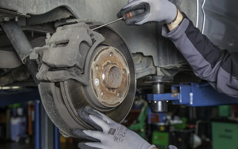 Mechanic in gloves using a screwdriver to replace a car's brake rotor and caliper on a lift Mechanic in gloves using a screwdriver to replace a car's brake rotor and caliper on a lift