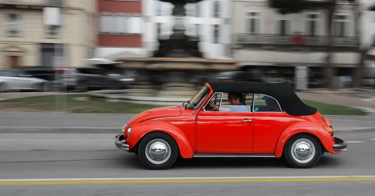 Red convertible with a black top driving past a fountain on a city street