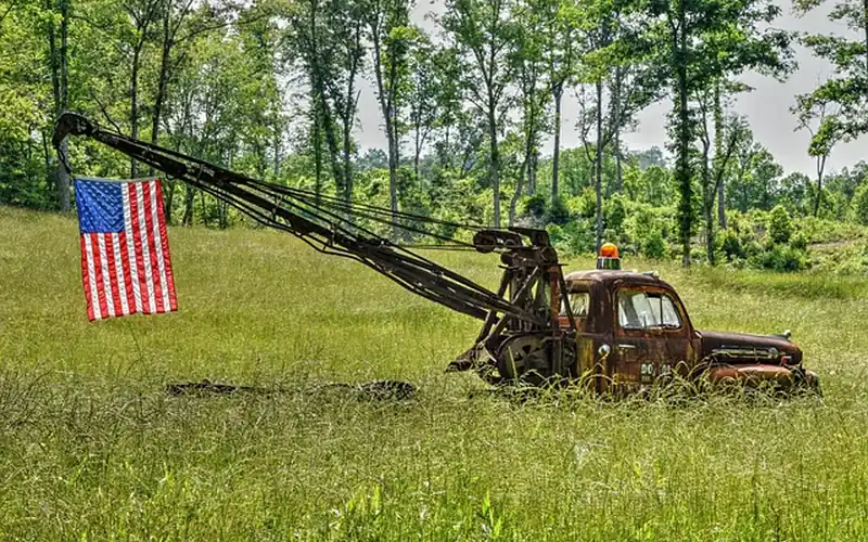 Rusty vintage tow truck with a raised boom parked in a grass field