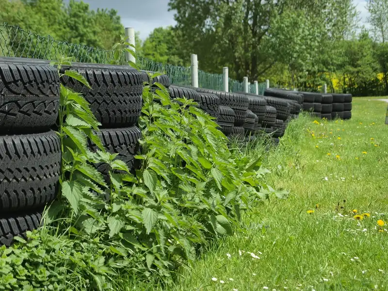 Rows of tires stacked outdoors along a fence in green grass