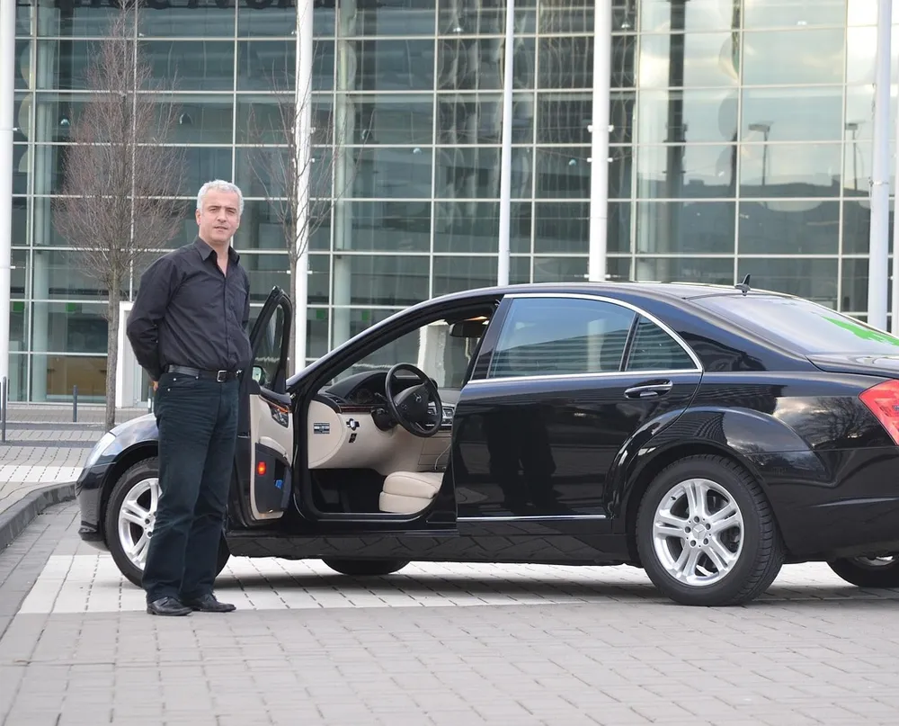 Man standing beside a black luxury sedan with the driver door open