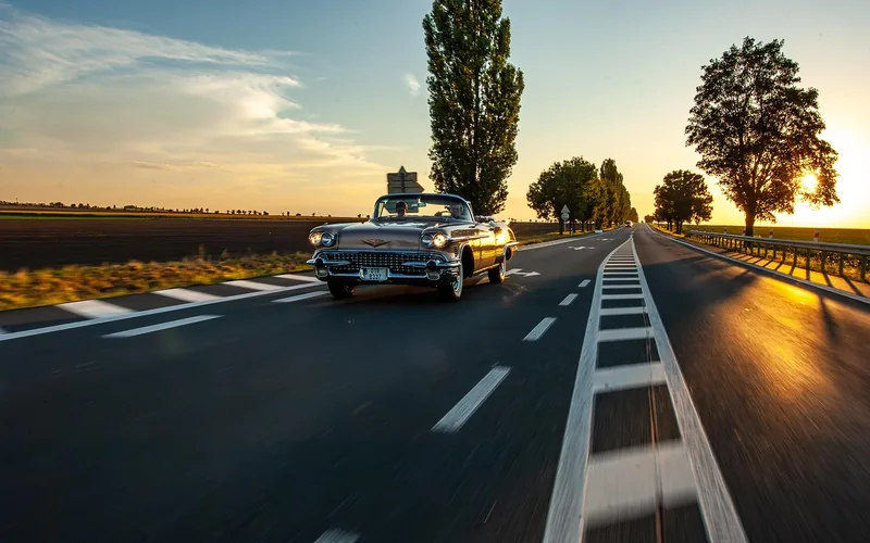 Vintage American convertible driving down an open road at sunset