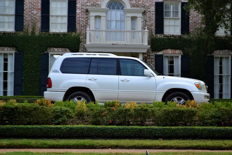 White SUV parked in front of a brick house with a hedge