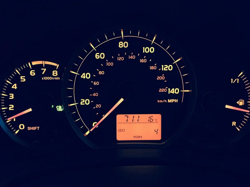 Car dashboard gauges showing the odometer reading in miles at night