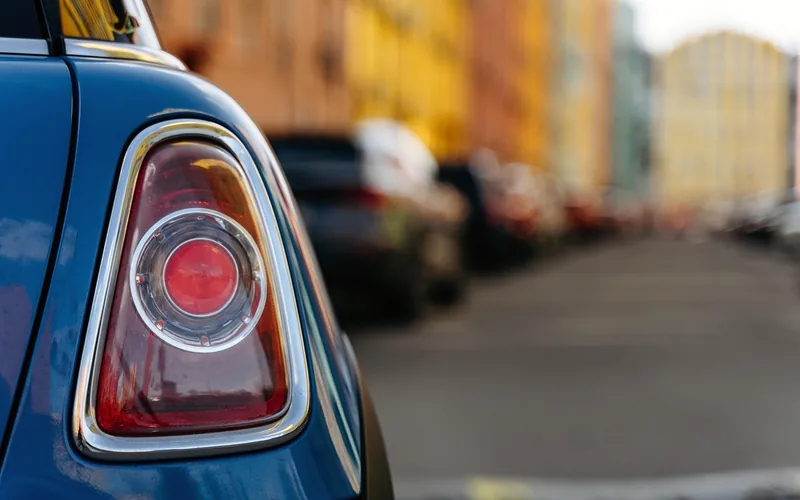 Rear taillight of a car parked on a residential street where pedestrians walk close behind vehicles