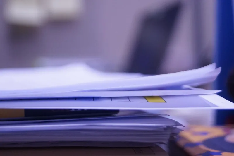 Stack of loose paper documents on an office desk in soft focus