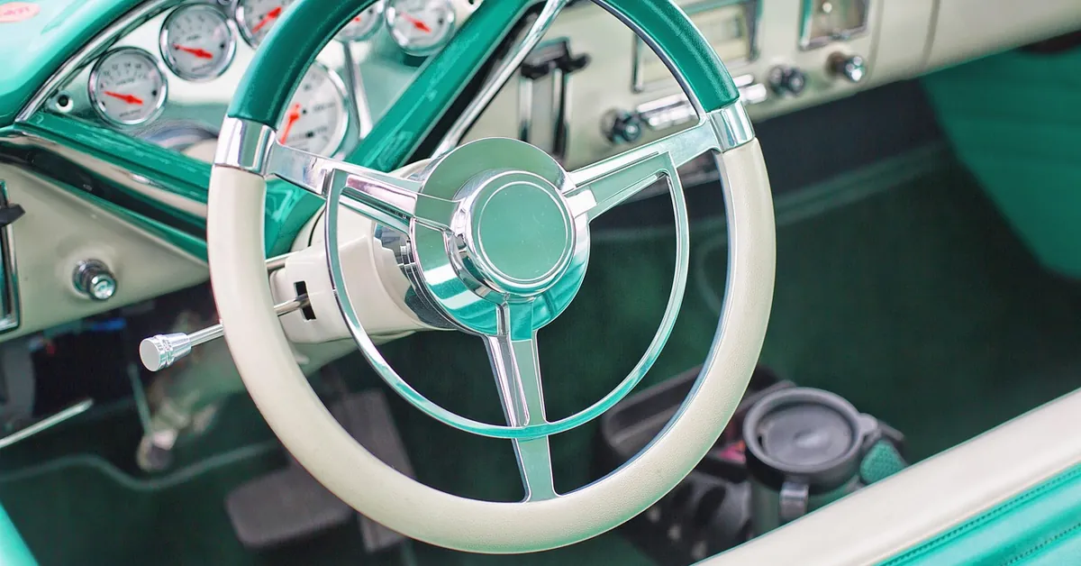Teal and cream vintage car steering wheel and dashboard gauges seen through the open door