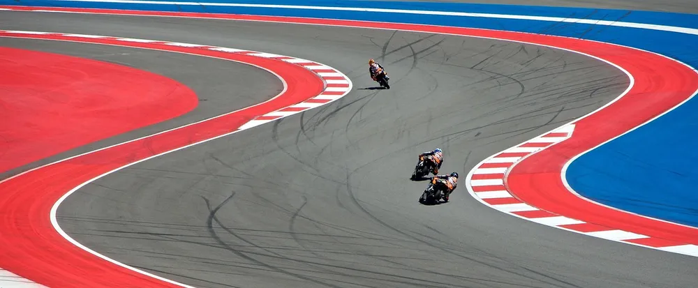 Three motorcycle riders leaning through a curve on a red and blue race circuit