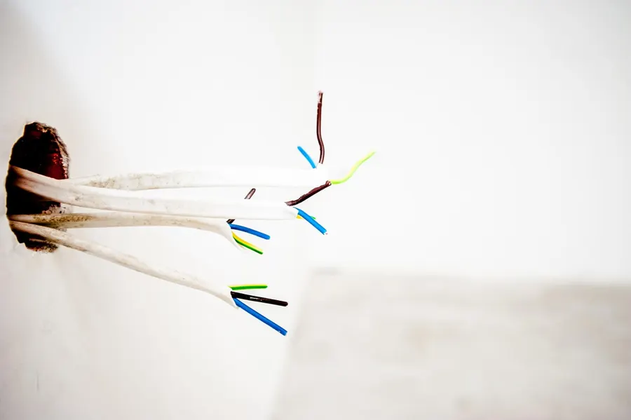 Insulated wires with stripped ends coming out of an opening in a white wall