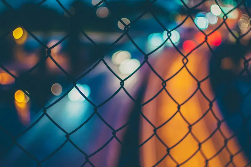 Out-of-focus colored night lights seen through a chain-link fence