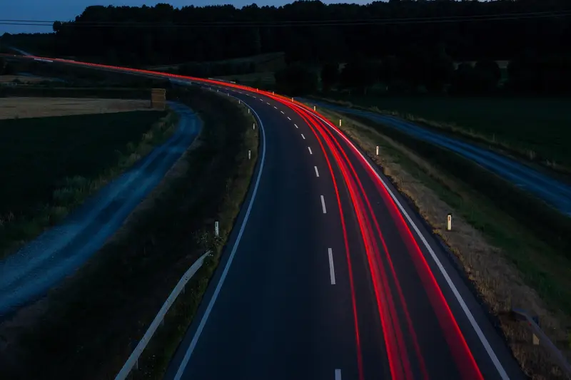 Red tail light trails along a curved road at dusk