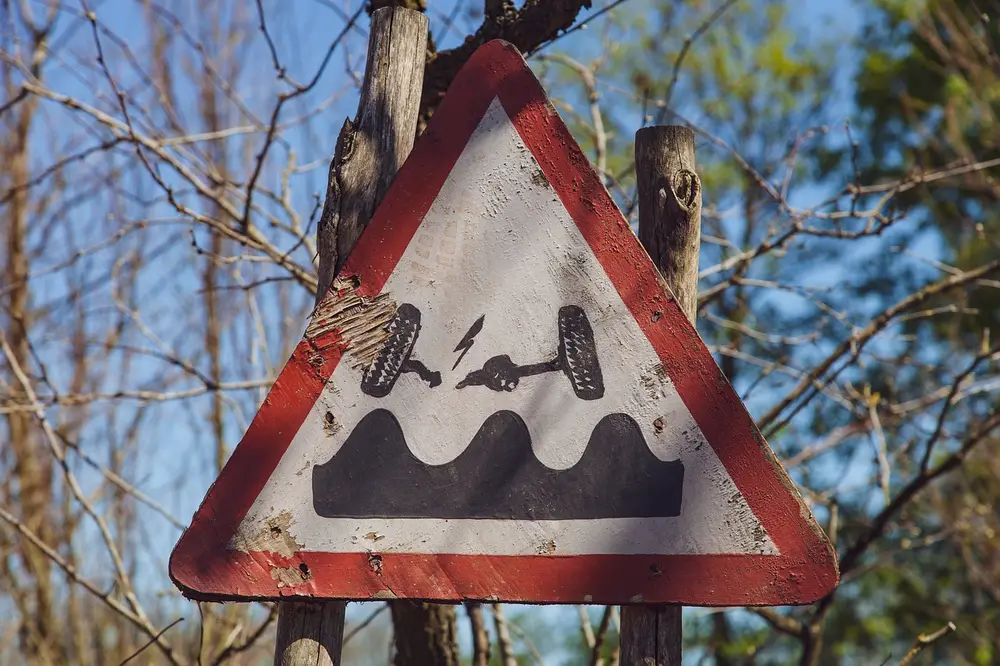 Weathered triangular road warning sign showing a car axle above a bumpy road