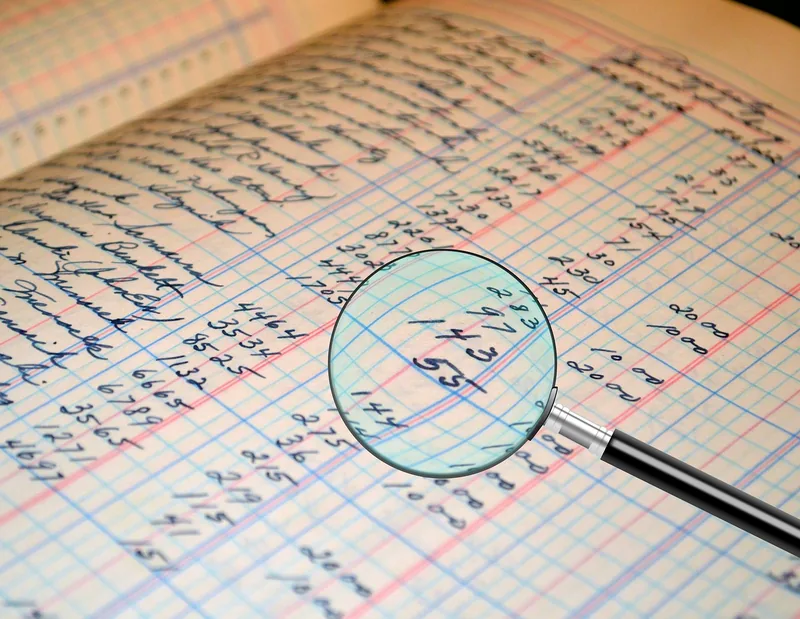 Handwritten accounting ledger columns viewed through a magnifying glass