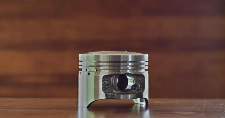 A clean aluminum engine piston with ring grooves standing on a wooden table
