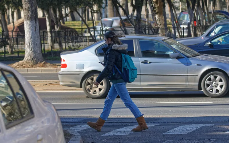 Pedestrian crossing a street between rows of parked cars in traffic